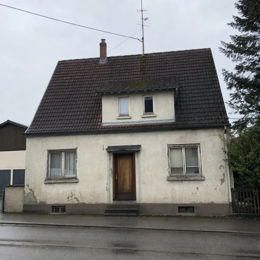 Unsaniertes Einfamilienhaus aus den 1960er-Jahren mit verwittertem Putz und alten Holzfenstern