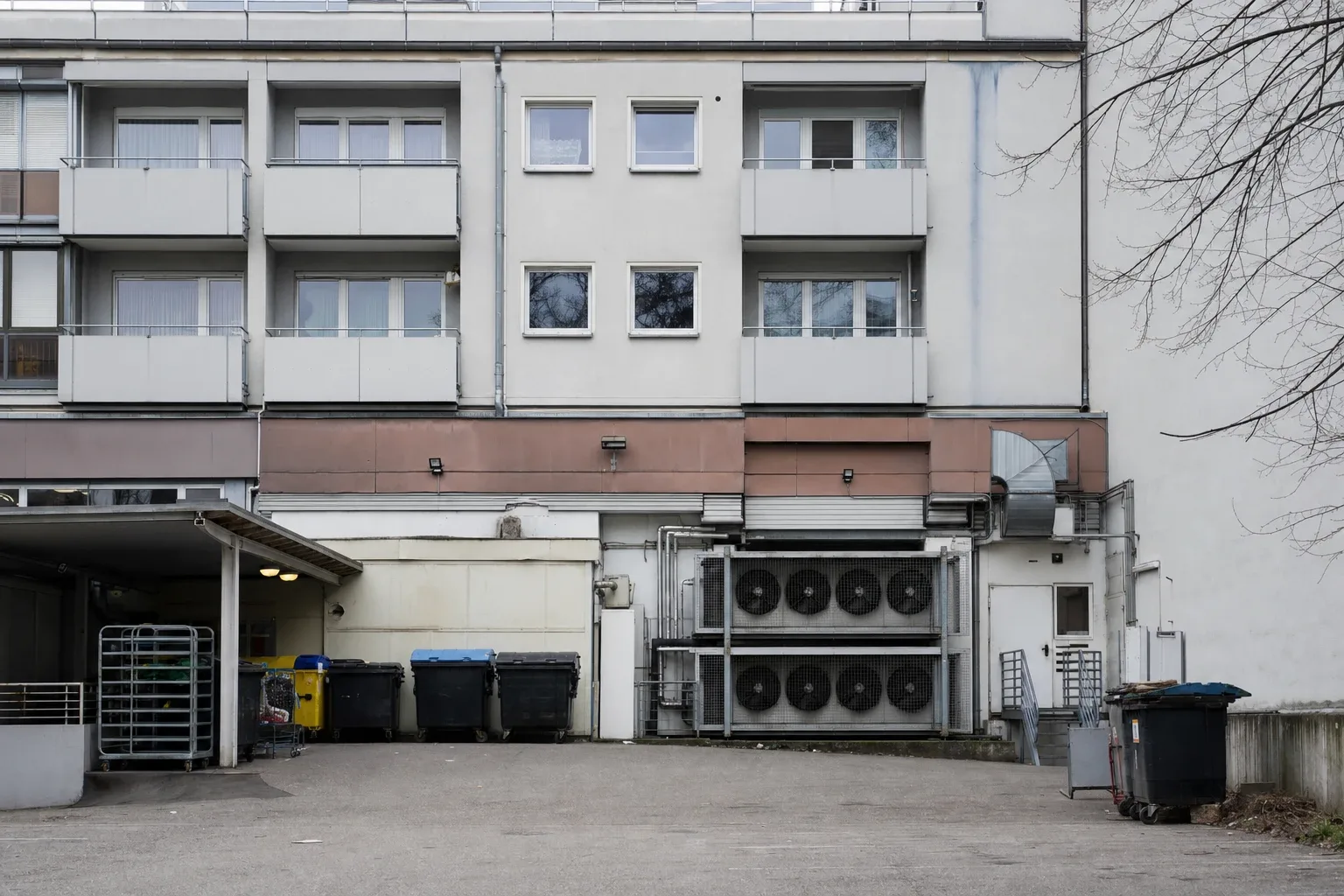 Rückseite eines Supermarkts mit großen Lüftungs- und Kühlaggregaten, darüber drei Etagen Wohnungen